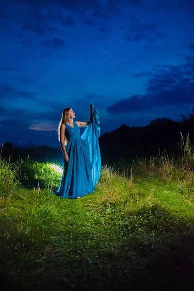 Mooie blonde model in lange blauwe lucht jurk poseren in Ray van licht — Stockfoto