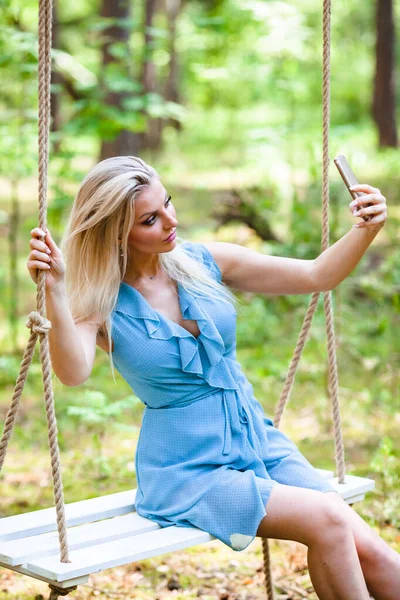 Красивая блондинка в синем платье с помощью смартфона делает селфи — стоковое фото