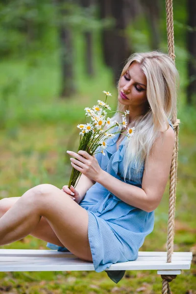 Красивая блондинка в синем платье позирует с букетом ромашки — стоковое фото