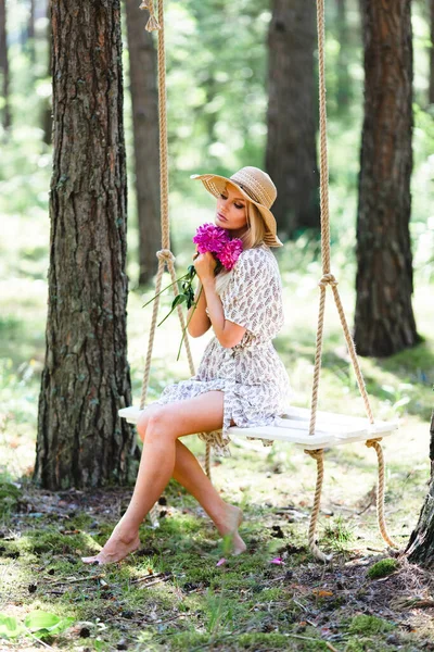 Красивая женщина в соломенной шляпе позирует с цветочным букетом на качелях — стоковое фото
