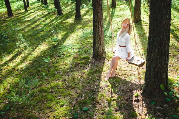 Блондинка с тонкими красивыми голыми ногами сидит на веревке качели — стоковое фото