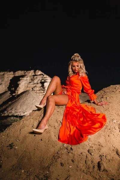 Blond kvinna i orange klänning poserar i bakgrunden av sand hill — Stockfoto
