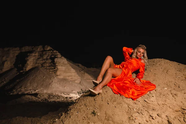 Blond kvinna i orange klänning poserar i bakgrunden av sand hill — Stockfoto