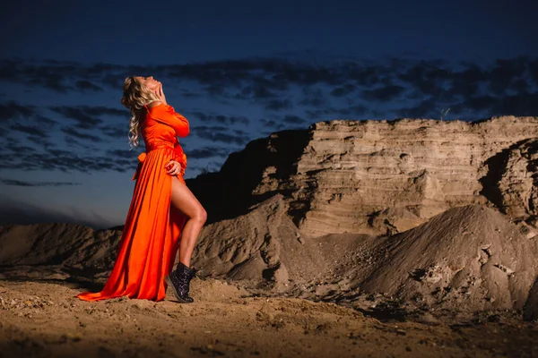 Kvinna i orange klänning poserar nära sand kulle i bakgrunden av solnedgången Stockbild