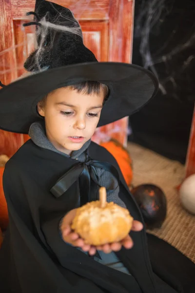 Caucasian boy in carnival wizard costume with decorative pumpkin on Haloween decor background. Halloween, carnival, masquerade, childhood, fairytale theme.