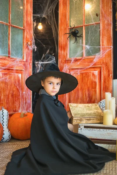Caucasian boy in carnival wizard costume reading magic book on Haloween decor background. Halloween, carnival, masquerade, childhood, fairytale theme.