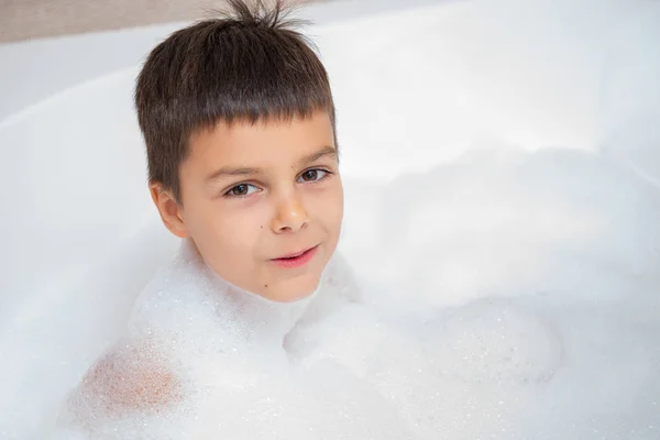 Smiling caucasian boy takes a bath with foam. Childhood, take a bath, hygiene theme.