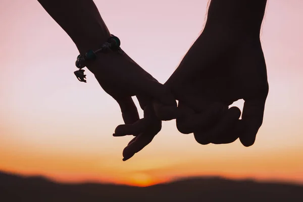 Silhouettes of female and male hands holding hands against background of setting sun. Relationships, love, date theme. Toned.