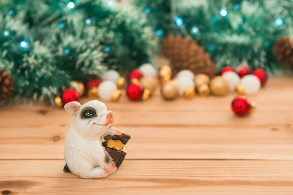 Small ceramic pig with money box on Christmas ornaments and lights background, selective focus. New year backdrop with copy space for cards, posters and invitation.