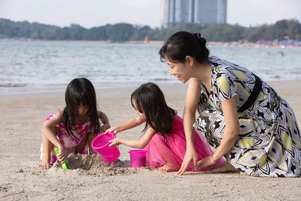 Asian Chinese mum and daughters playing sand together at beach outdoor
