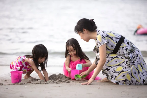 Asian Chinese mum and daughters playing sand together at beach outdoor