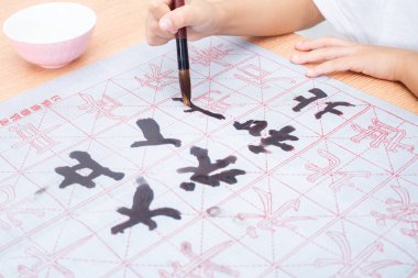 Close up of children hands holding brush to practice Chinese calligraphy at home clipart