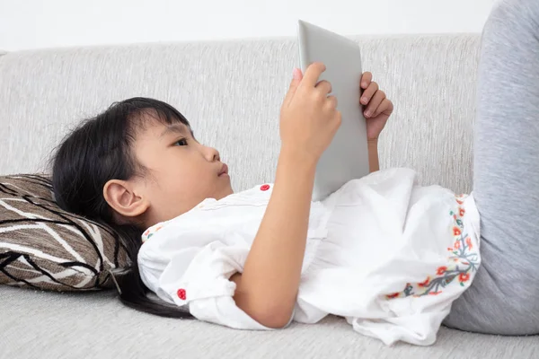 Kanepede yatan ve tablet oturma odasında oynarken Asyalı Çinli küçük kız
