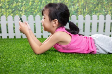 Asyalı küçük Çinli kız cep telefonu ile açık parkta oynarken