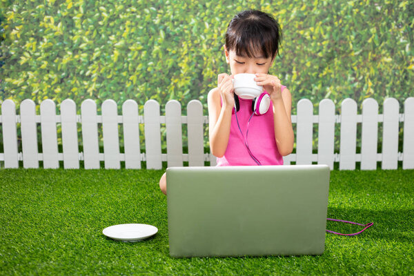 Asian Little Chinese girl sitting on the grass and playing with laptop at outdoor park