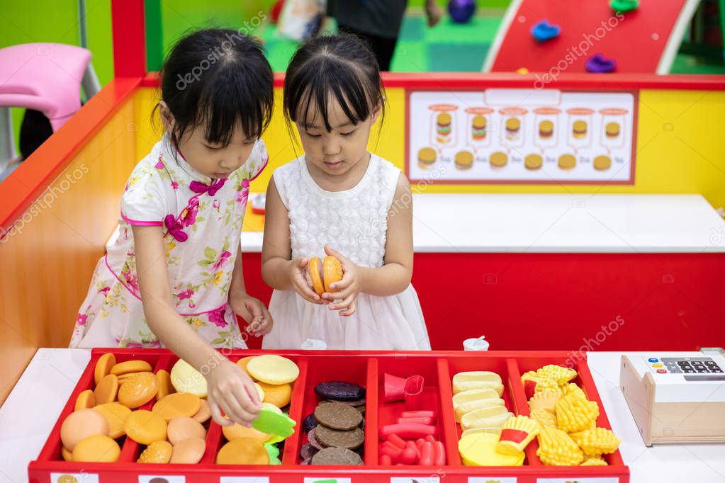 Asian Chinese little sisters role-playing at burger store at indoor playground