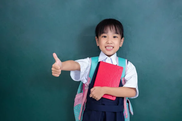 亚洲中国的小女孩在制服显示竖起大拇指反对绿色黑板在课堂上 — 图库照片