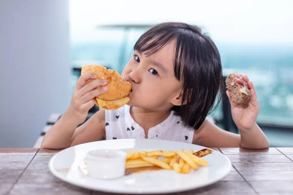 Asiatiskapojke liten kinesisk flicka äter hamburgare Stockbild