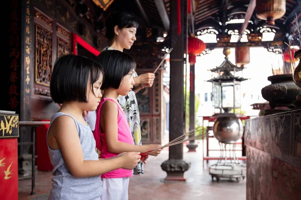 Asian Little Chinese Sisters and mother praying with burning inc Royalty Free Stock Images
