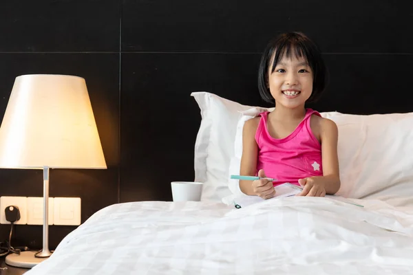 Asiatico piccolo cinese ragazza doing homework in letto — Foto Stock