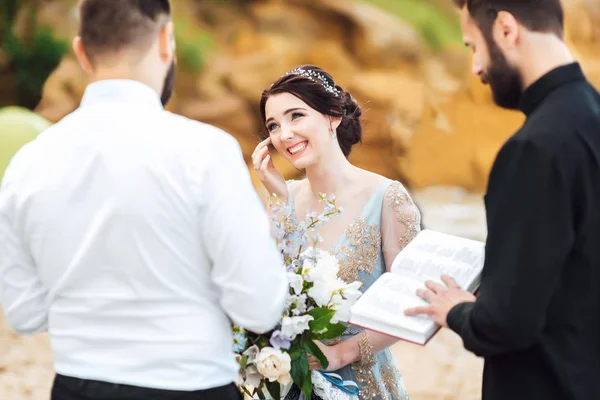 Casal de casamento no oceano com um padre — Fotografia de Stock