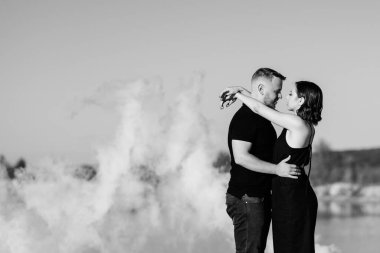 Siyah elbiseli bir adam ve bir kız beyaz bir dumanın içinde sarılıyorlar.