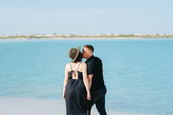 一对年轻夫妇和一个穿黑衣服的女孩在蓝水边的白沙滩上散步 — 图库照片
