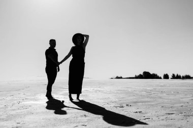 Genç çift, bir adam ve siyah elbiseli neşeli bir kız kar beyazı çölünde yürüyorlar.