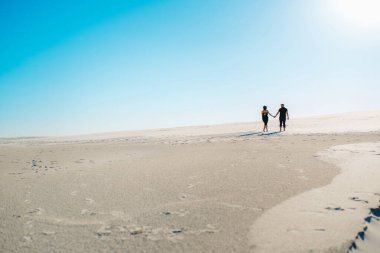 Genç çift, bir adam ve siyah elbiseli neşeli bir kız kar beyazı çölünde yürüyorlar.