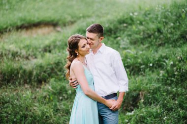 Beyaz gömlekli mutlu bir adam ve turkuaz elbiseli bir kız, gelin ve damat orman parkında yürüyorlar.