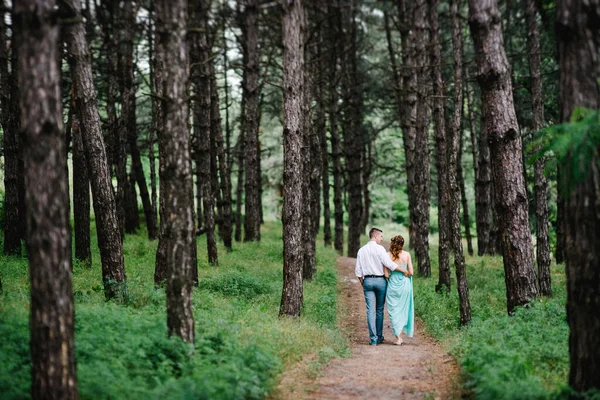 白いシャツを着た幸せな男とターコイズブルーのドレスを着た女の子花嫁と新郎が森林公園を歩いています — ストック写真