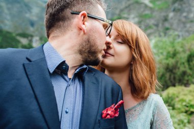 Genç bir çift göl kenarında yürüyüş yapıyor. Etrafı Karpat dağlarıyla çevrili.