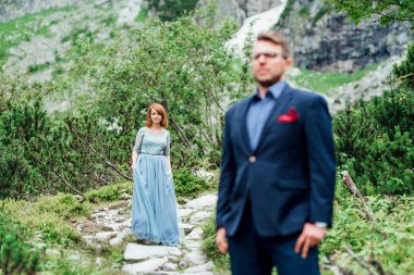 Genç bir çift göl kenarında yürüyüş yapıyor. Etrafı Karpat dağlarıyla çevrili.