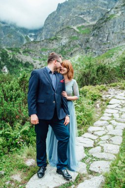 Genç bir çift göl kenarında yürüyüş yapıyor. Etrafı Karpat dağlarıyla çevrili.