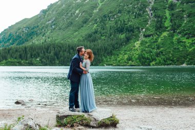 Genç bir çift göl kenarında yürüyüş yapıyor. Etrafı Karpat dağlarıyla çevrili.