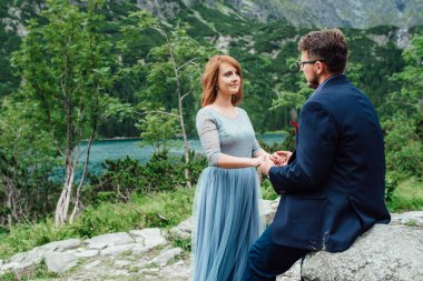 Genç bir çift göl kenarında yürüyüş yapıyor. Etrafı Karpat dağlarıyla çevrili.