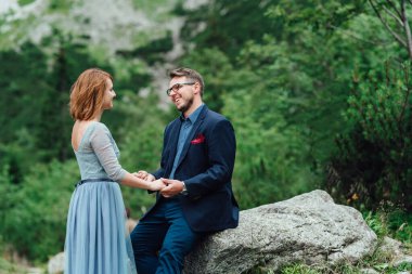 Genç bir çift göl kenarında yürüyüş yapıyor. Etrafı Karpat dağlarıyla çevrili.