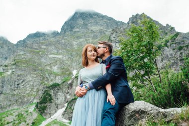 Genç bir çift göl kenarında yürüyüş yapıyor. Etrafı Karpat dağlarıyla çevrili.