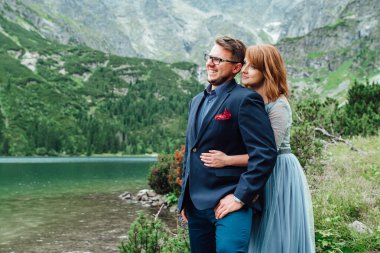 Genç bir çift göl kenarında yürüyüş yapıyor. Etrafı Karpat dağlarıyla çevrili.