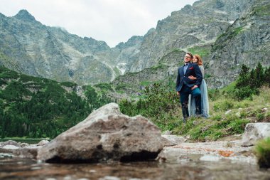 Genç bir çift göl kenarında yürüyüş yapıyor. Etrafı Karpat dağlarıyla çevrili.
