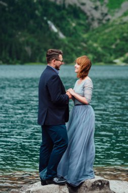 Genç bir çift göl kenarında yürüyüş yapıyor. Etrafı Karpat dağlarıyla çevrili.