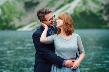 Genç bir çift göl kenarında yürüyüş yapıyor. Etrafı Karpat dağlarıyla çevrili.