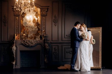 Genç bir çift karanlık bir stüdyoda, bir ayna ve bir avizeyle.