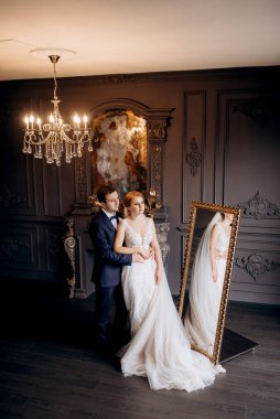 Genç bir çift karanlık bir stüdyoda, bir ayna ve bir avizeyle.