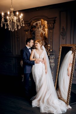 Genç bir çift karanlık bir stüdyoda, bir ayna ve bir avizeyle.