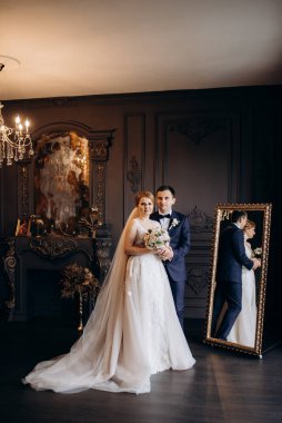 Genç bir çift karanlık bir stüdyoda, bir ayna ve bir avizeyle.