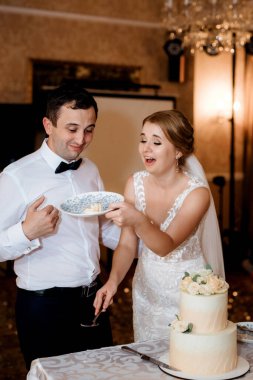 newlyweds happily cut, laugh and taste the wedding cake