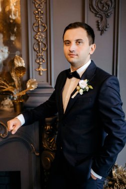 Karanlık bir stüdyoda, aynalı ve avizeli genç bir damat.