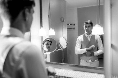 Üç parçalı takım elbiseli bir damat sabah bir otel banyosunda aynalı bir düğüne hazırlanır.