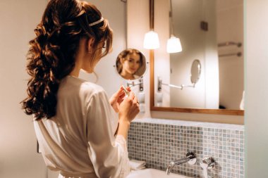 bride in a veil with makeup paints her lips in the bathroom